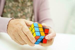 Bangkok, Thailand - May 15, 2022 Asian elderly woman playing Rubik cube game to practice brain training for help dementia prevention and Alzheimer disease. photo