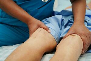 Doctor checking Asian elderly woman patient with scar knee replacement surgery in hospital. photo