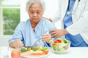 Asian elderly woman patient eating salmon stake and vegetable salad for healthy food in hospital. photo