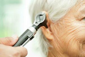 Otolaryngologist or ENT physician doctor examining senior patient ear with otoscope, hearing loss problem. photo