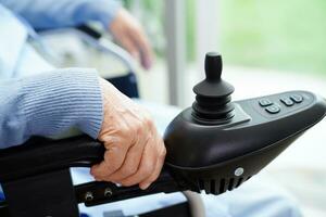 Asian elderly woman disability patient sitting on electric wheelchair in park, medical concept. photo