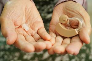 Asian senior woman patient using hearing aid in ear to reduce hearing loss problem. photo