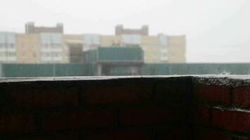 regndroppar droppande på de balkong räcke. tak av hus i en bostads- område i de bakgrund. video