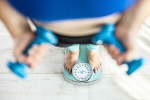 Heavy fat woman stands on a scale and holds dumbbells in her hands photo