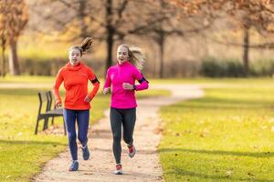 hermosa dos mujer corriendo fuera de en soleado otoño parque foto