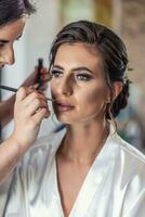 Makeup artist applying make-up on a face of a beautiful bride photo