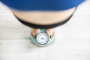 un obeso mujer soportes en un escala y pesa más que 100 kilogramos foto