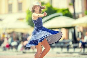 Beautiful cute young girl dancing on the street from happiness.Cute happy girl in summer clothes dancing in the sun. photo