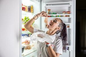 Very hungry woman in pajamas enjoying ham at night by the fridge photo