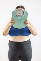 A very overweight woman holds a scale showing her weight in front of her head photo