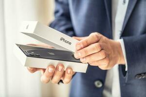 Businessman in suit holding in hands and opening a box with a brand new black apple iphone 12 photo