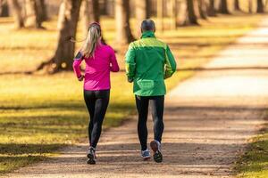 Rear view of a two runners, young woman and one mature man running in an autumn park photo