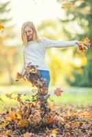 retrato de un joven mujer disfrutando el otoño atmósfera y jugando desde arce hojas en parque foto