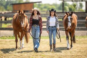 Two cowgirls confidently walk their paint horses towards the camera photo