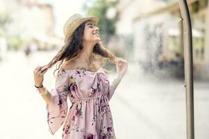 A cute young lady is relaxing from the heat under a water shower in the city center photo