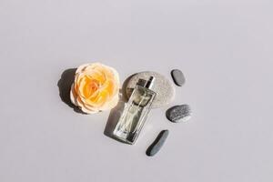 A chic bottle of feminine perfume or cosmetic spray lies on a gray oval sea stone with a fresh rose flower. Top view. The concept of beauty. photo