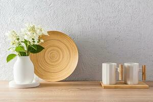 Stylish light kitchen background with two white mugs, a vase of flowers, a bamboo dish. front view. minimalism. photo