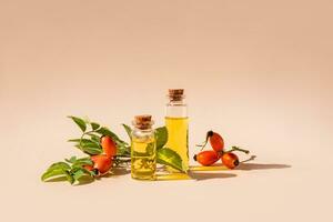 Two glass bottles with a stopper with natural rosehip oil on a beige background with rosehip branches with fruits. front view. photo