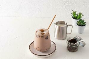 A large beautiful glass of iced coffee latte. Fashionable metal jug of milk. Potted plants. White textured background. A copy of the space. photo