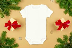Christmas white baby girl or boy bodysuit mockup flat lay with gift boxes and xmas tree branches on paper background. Design onesie template, print presentation mock up. Top view. photo