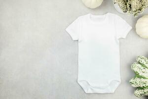 White baby girl or boy bodysuit mockup flat lay with pumpkins on gray concrete background. Design onesie template, print presentation mock up. Top view. photo