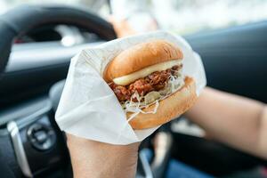 asiático dama participación hamburguesa a comer en auto, peligroso y riesgo un accidente. foto