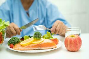 asiático mayor mujer paciente comiendo salmón filete desayuno con vegetal sano comida en hospital. foto