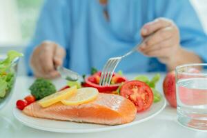 Asian elderly woman patient eating salmon steak breakfast with vegetable healthy food in hospital. photo