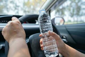 Asian woman driver holding bottle for drink water while driving a car. Plastic hot water bottle cause fire. photo