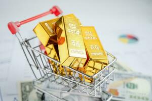 Gold bar in shopping cart on US dollar banknotes money and graph, economy finance exchange trade investment concept. photo