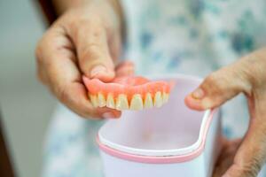 Asian elderly woman patient holding to use denture, healthy strong medical concept. photo