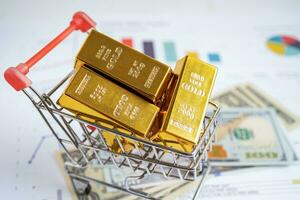 Gold bar in shopping cart on US dollar banknotes money and graph, economy finance exchange trade investment concept. photo