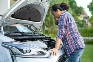 Asian woman check for repair under the hood of broken down car on the side of the road. photo