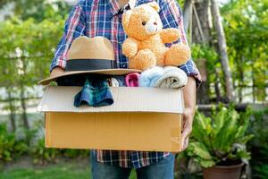 Volunteer woman provide clothing donation box with used clothes and doll to support help for refugee, homeless or poor people in the world. photo