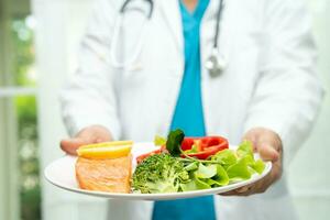 Nutritionist doctor holding healthy salmon steak and vegetable vitamin food for patient in hospital. photo