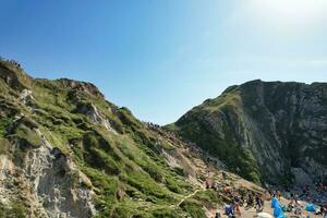 alto ángulo ver de personas son que se acerca a durdle puerta playa cuales es más famoso turista atracción sitio mediante caminando distancia terminado paisaje y sierras. capturado en septiembre 9, 2023 foto