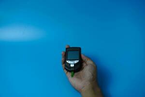Man checking blood sugar level using glucometer. Diabetes concept on blue background photo