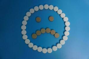 negative smile made of pills, tablet, capsule on blue background. Concept of medicine, pills, treatment, medical insurance. sad concept photo