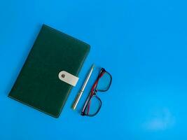 top view blank green leather diary, pen and glass on blue background photo