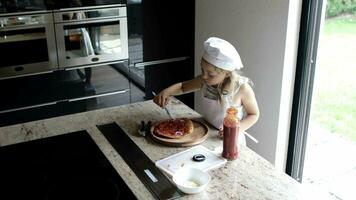flicka av 6 år gammal är framställning pizza med tomater sås och violett lök i främre av henne abonnenter. video
