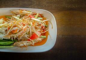 Papaya salad cooked with cowpea, peanut, carrot, lemon, chilis and sugar on white plate food long beans Wood Table Texture. photo