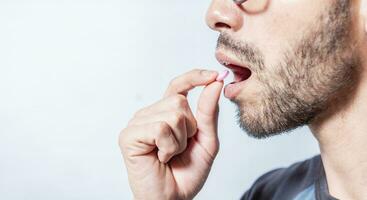 Close-up of a man taking an aspirin. Person taking a pill isolated, Close up of young man putting a pill in his mouth. Self-medication concept, Man putting a pill in his mouth isolated photo