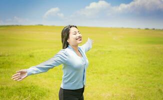 Young woman smiling and spreading her hands in the green field, concept of woman breathing fresh air in the field, Happy woman breathing fresh air in the field and spreading arms photo