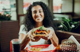 Happy girl showing burger in a restaurant. Close-up of a girl showing appetizing hamburger in a restaurant photo