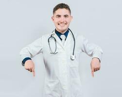 Young doctor pointing a promotion down. Happy doctor pointing fingers down. Latin doctor pointing down an isolated advertising space photo