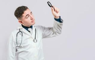 Doctor looking for something with magnifying glass looking isolated. Handsome Doctor holding magnifying glass and looking for something photo