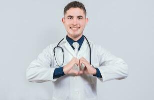 Friendly doctor making heart gesture with hands isolated. Young latin doctor making heart shape on isolated background photo