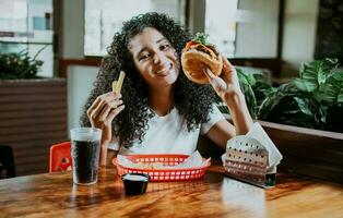 Afro young woman enjoying a hamburger with fries in a restaurant. Happy girl enjoying a hamburger in a restaurant photo