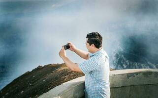 joven turista hombre tomando fotos a un volcánico punto de vista. aventurero hombre con su célula teléfono tomando fotos a un punto de vista, turista hombre tomando fotos a un punto de vista