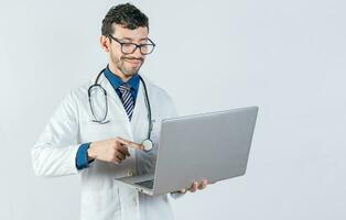 Young doctor in glasses using notebook on isolated background. Handsome doctor using laptop isolated. Smiling doctor standing using laptop isolated photo